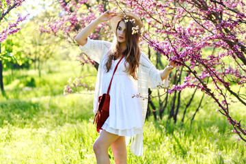 Naklejka na ściany i meble Charming pretty young woman with long hair in summer hat, white light dress walking in sunny garden