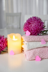 Set of fresh towels of pink and white color with purple aster flowers, candle and pink hearts on white table. Spa or massage salon concept. Romantic surprise for Valentine`s Day.