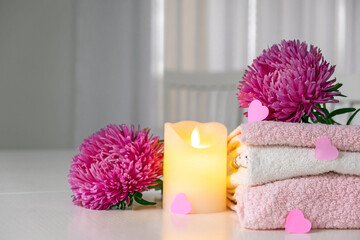 Obraz na płótnie Canvas Set of fresh towels of pink and white color with purple aster flowers, candle and pink hearts on white table. Hotel spa and wellness concept. Valentine Day. Copy space.
