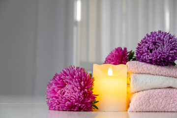 Set of fresh towels of pink and white color with purple aster flowers and candle on white table. Spa and wellness or beauty salon concept. Copy space.