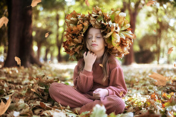 A cute little girl with a wreath of leaves on her head in a park one autumn day