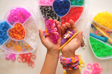Loom for weaving toy bracelets from elastic bands in the hands of a girl. A popular hobby for children. Containers for storing rubber bands for weaving. Knitting rubber bands with loom