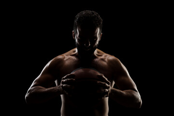 Obraz na płótnie Canvas Basketball player holding a ball against black background. Side lit muscular Caucasian man silhouette