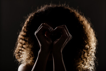 Beautiful brunette girl with long curly hair. Hearth shaped hands. Studio silhouette portrait on...