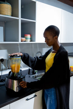 Young African American woman wearing a yellow shirt making a smoothie in her home kitchen
