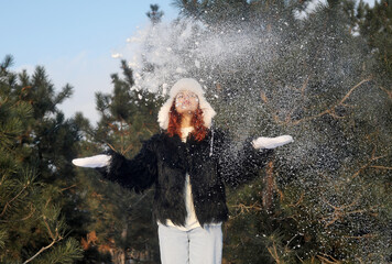 Young beautiful red haired woman in hat has fun outdoors with snow. Woman walking in the wood in...