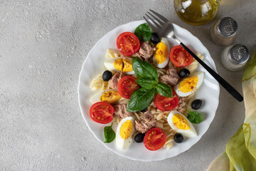 Canned tuna salad with pasta, cherry tomatoes, black olives, boiled egg and basil. Healthy food. View from above.