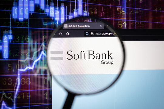 SoftBank company logo on a website with blurry stock market developments in the background, seen on a computer screen through a magnifying glass	