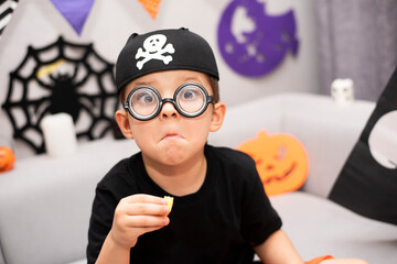A funny surprised boy in a pirate costume eats sweets with a funny expression and round nerd...