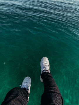 Feet and legs dangling over aqua water