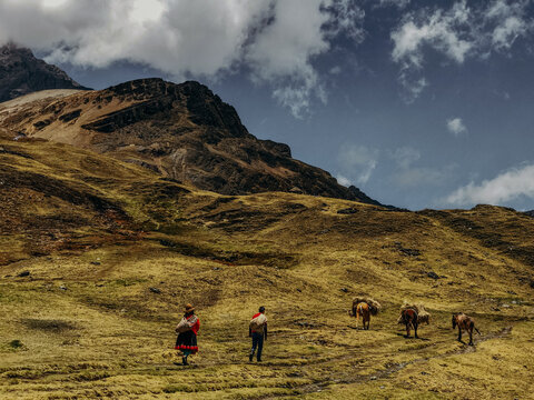 Peruvian mountain with blue sky and clouds and people carrying things in foreground