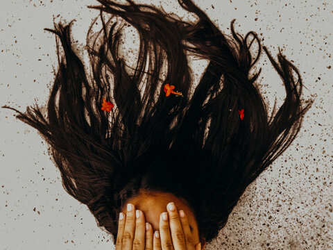 Girl with dark hair and three red flowers covering her face with her hands