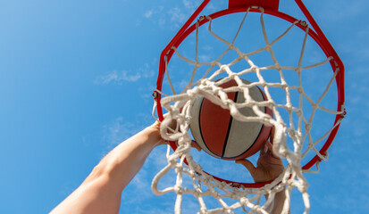 man dunking basketball ball through net ring with hands, sport © Olena