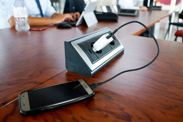 A mobile phone is charge into a socket on a table in a European work office.