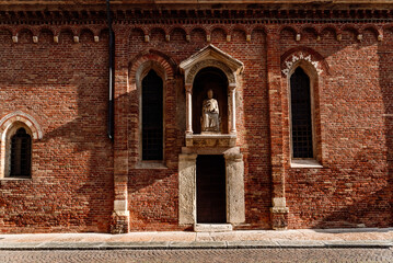 Brick facade in the afternoon sun of a religious Veronese hermitage with a statue of a saint.