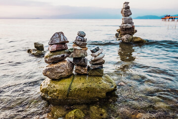 Small mountains of stones in columns created by tourists on the shore of a lake at sunset.