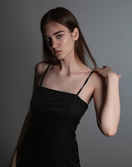 Naklejka premium Beautiful woman with nude makeup and volume brown long hair looking mystery in black dress on grey background. Closeup. Art