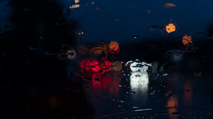 Abstract an blurred of rainny ripples on the glass of car. With bokeh light of front and back of other car at night.