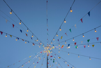 Garland with colorful pennants and light bulbs on pole over blue sky