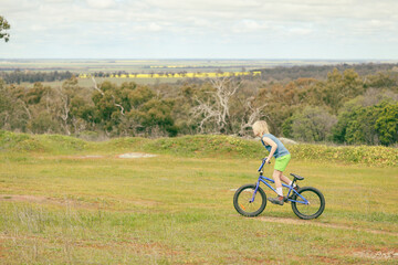 Fototapeta na wymiar Boy riding bike in on hill with canola field in background
