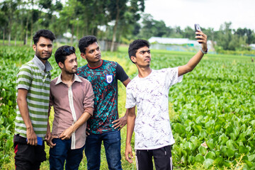 Four young boys are standing in the middle of green nature and taking pictures of themselves with mobile phones in their hands. the background blur