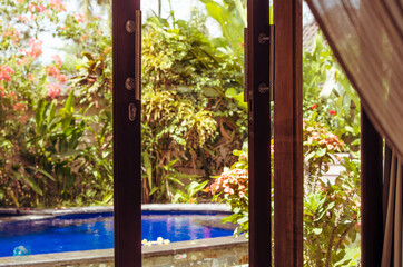Small swimming pool behind window in green garden