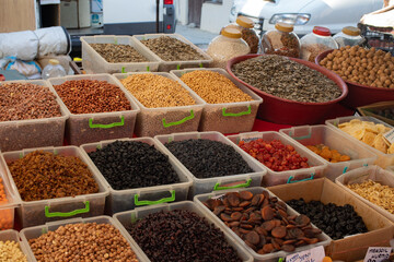 A colorful and neatly arranged selection of dried fruits, nuts, and seeds at a local market. Various types of raisins, apricots, almonds, sunflower seeds, and legumes are displayed in containers.