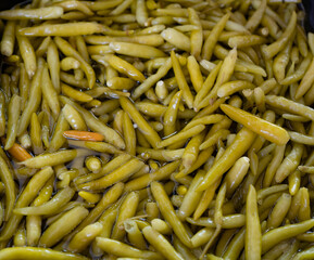 Close-up of pickled green beans soaked in brine. The vibrant, glossy texture of the beans...