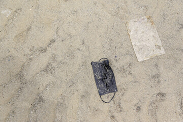 Surgical face mask and plastic bag leave as garbage on sea sand. Concept of environmental pollution impact form coronavirus covid 19 pandemic.