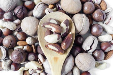 brazil nuts in a wooden spoon on the background of a scattering of different nuts, assorted nuts	