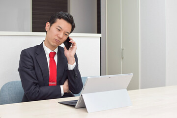 A young Asian man during telework at home talks on his phone and thinks about how to answer to his client