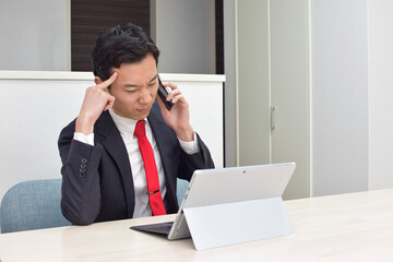 A young Asian man during telework at home talks on his phone and thinks about how to answer to his client