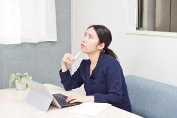 A young Asian woman thinks about her tasks and puts her pen on her face during telework