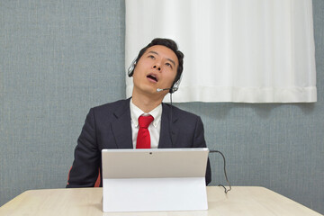 A young Asian man with a headset wearing business suit is stunned during telework at home