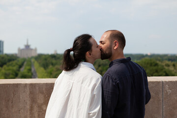 Fototapeta premium Romantic couple celebrating relationship anniversary kissing on tower terrace enjoying spending time together during vacation. View of city skyline from observation point. Panoramic view of buildings