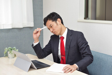 Naklejka premium A young Asian man during telework at home thinks about new idea using a pen and a notebook