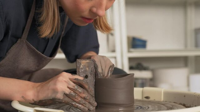 4K Asian woman sculptor artist hands sculpture clay on pottery wheel at ceramic studio. Female craftsman molding raw clay create pottery shapes at workshop. Small business handicraft product concept.