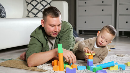 Young father in green shirt and little clever son play building tower using colorful wooden blocks...
