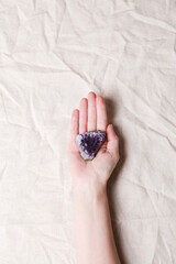 druse raw purple amethyst crystal on piece of stone on woman hand on grey linen