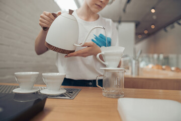 Female barista pouring boiled water through filter into cup