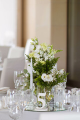 White tablecloths with clear vases and white flowers and fern arrangements. Golden colored plates, peavh napkins, table numbers and mirror centerpieces.