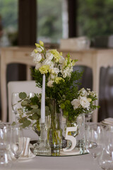 White tablecloths with clear vases and white flowers and fern arrangements. Golden colored plates, peavh napkins, table numbers and mirror centerpieces.