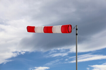 close up of red and white windsock indicator on cloudy sky