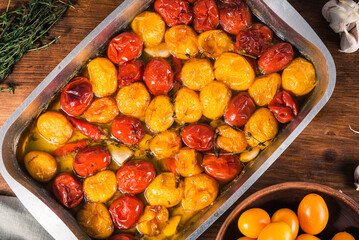 Confit of red and yellow cherry tomatoes with garlic, pepper and thyme in a baking sheet with olive oil, top view