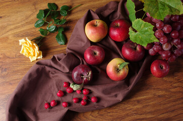 Apples, grapes and a yellow rose on a wooden table.