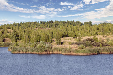 A lake with a plane surface and reflections against the blue sky and white clouds. Originated from an old quarry flooded, groups of islands overgrown with reeds.