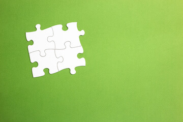 four white jigsaw pieces fitted together to form a group joined on all sides. green background. copy space. working set. space for letters and text.