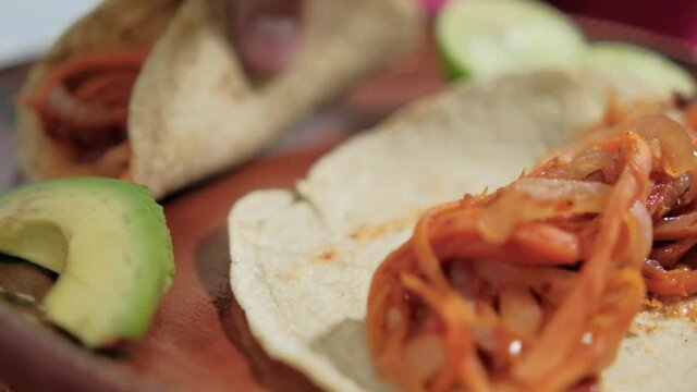 Hand holding vegan Mexican tinga tacos on traditional clay plate