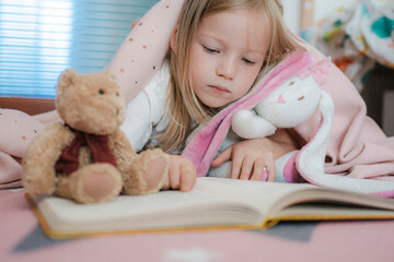 little girl in a pink children's room reads a book. cozy children's room with toys. room for girls