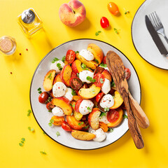 Summer peach Caprese salad with mozzarella and cherry tomatoes. Yellow background. Top view.	